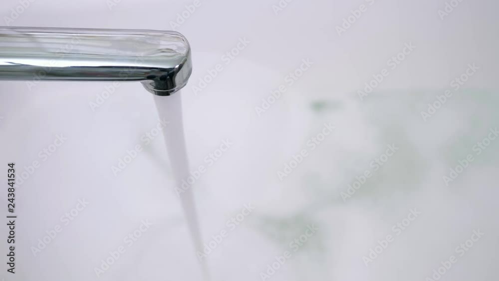 close up of water flows from the tap, bath with foam on the background close up of water flows from the tap, bath with foam on the background