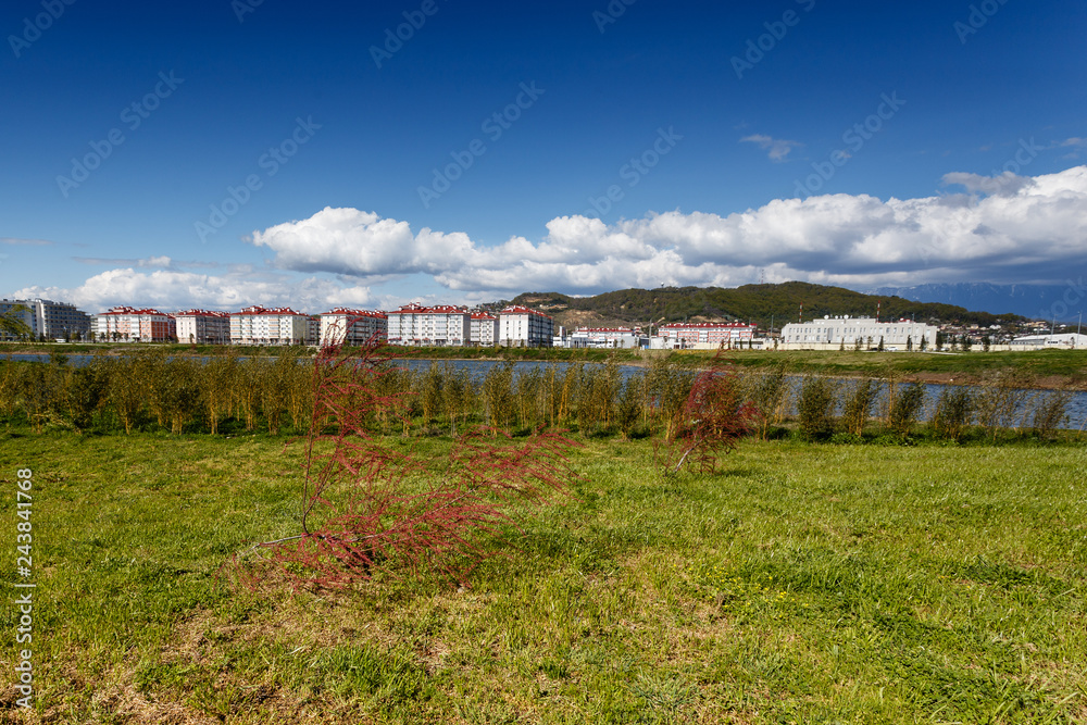 Obraz premium Adler, Sochi, Russia. Construction of Imereti lowland hotels and apartments. Red bush on a green lawn on the background of new buildings, mountains and white clouds