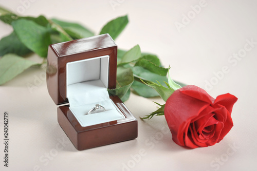 Ring with a diamond in a gift box. Next to the box is a red rose. The perfect holiday gift. Light background. Close-up. Macro shooting.... © Elena