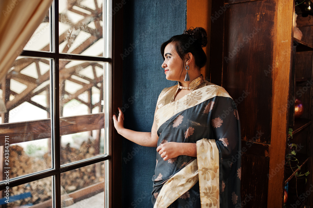 Elegant brunette south asian indian girl in saree posed indoor cafe against window. Elegant brunette south asian indian girl in saree posed indoor cafe against window.
