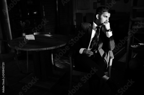 Elegant south asian indian business man in black suit posed indoor cafe in sun shadows.