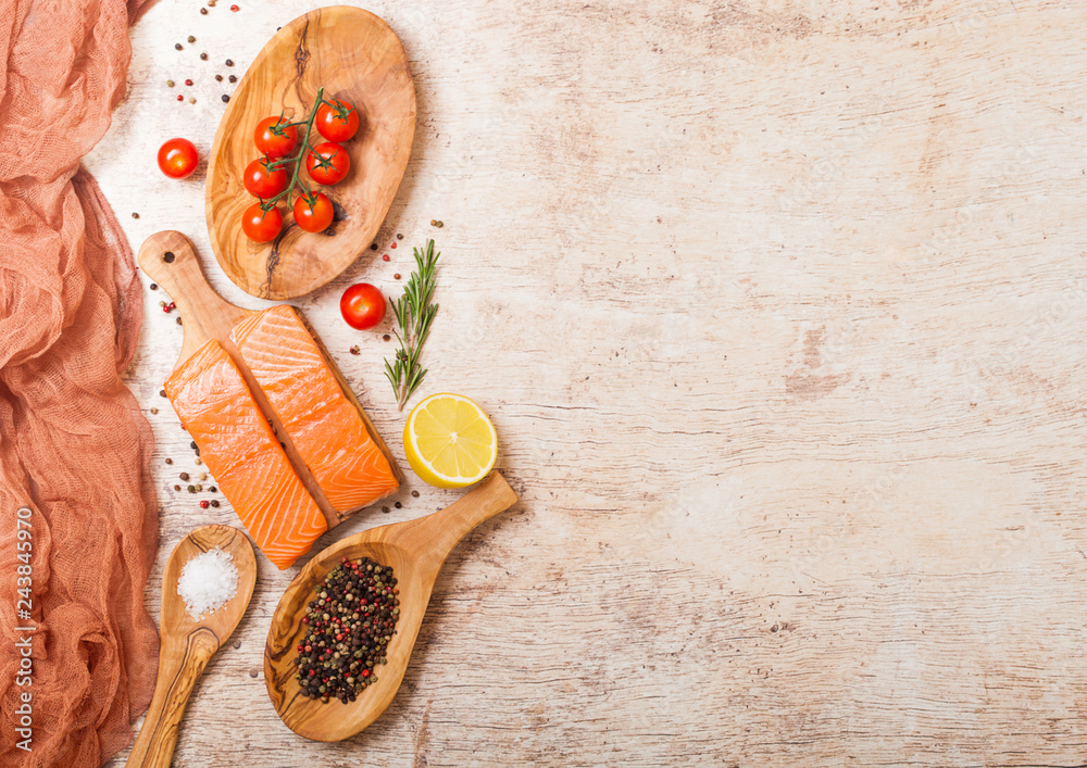 Fresh raw salmon slice on chopping board with pepper tomatoes and lemon on wooden kitchen table background. Olive wood bowl and plate