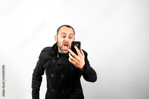 Middle-aged man with overcoat screams angrily at his mobile phone, isolated on white.