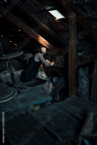 Girl with black dress looking up in an attic.