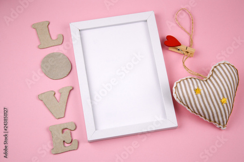 empty white frame with place for text ,letetrs  L O V E and fabric stuffed toy in a shape of heart on a pastel pink background photo