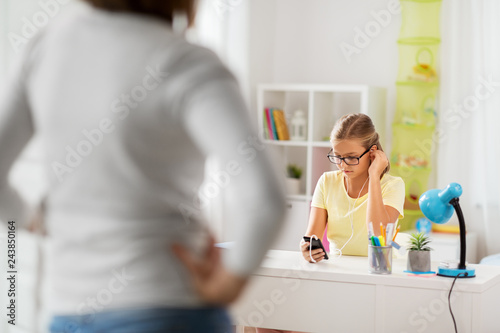 education  technology and school concept - daughter with smartphone distracting from homework and mother entering kids room