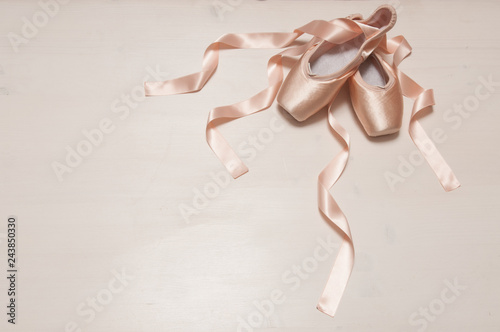 Pair of two satin ballet shoes with long ribbons lying on a white wooden background