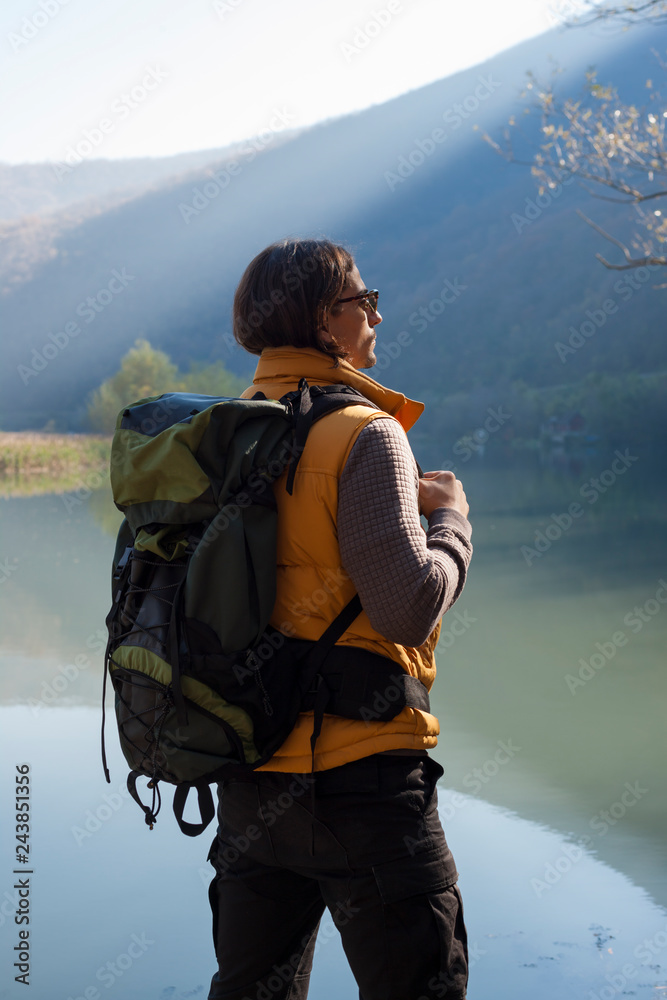 Man with backpack standing by the beautiful lake landscape.