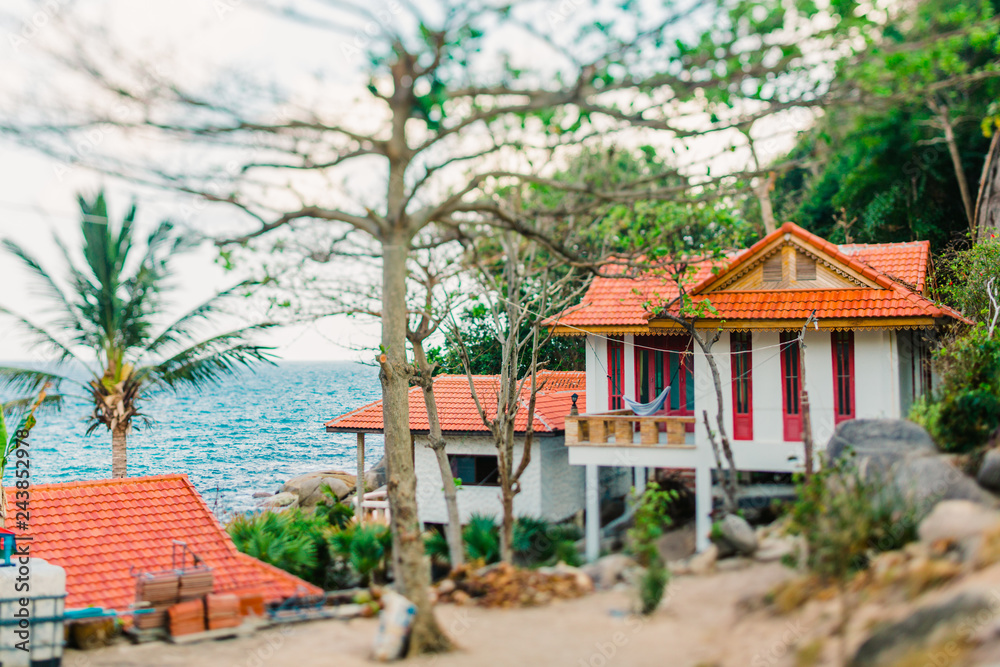 Bungalow on a tropical island in Thailand. House on the ocean with a red roof. Hammock hanging on the balcony. The ocean in the background. Shot on a tilt shift lens