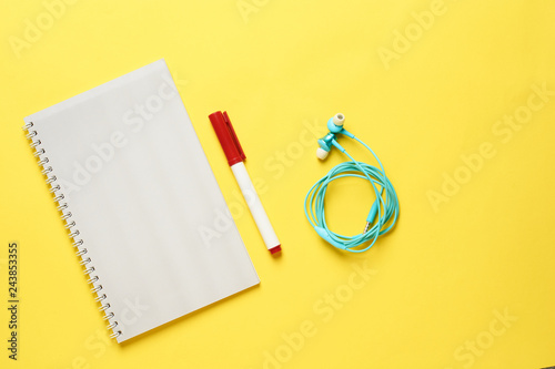 Top view of white paper blank notepad with marker and headphones on yellow paper background. Top view or flat lay. Copy space for text. Vertical.