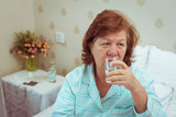 Senior woman drink medicine in bed.