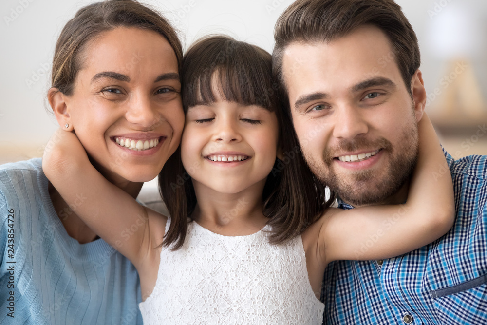 Cute little child daughter embracing caring parents mom and dad looking