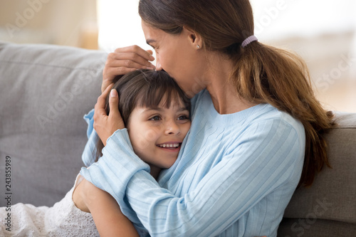 Loving single mother hugging cute little daughter kissing kid sitting on sofa, happy woman mum caressing embracing preschool girl, moms care and support, sincere warm relationships for child concept photo