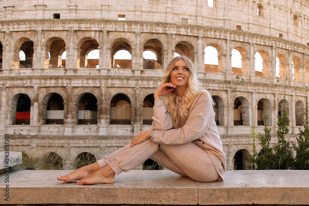 Naklejka premium piękna dziewczyna z długimi blond włosami w przytulnych ubraniach w pobliżu Koloseum w Rzymie