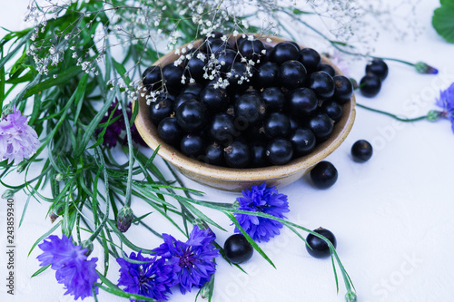 Fresh berries of black currant in a plate on a table together with cornflowers . For a diet and saturation with vitamins photo