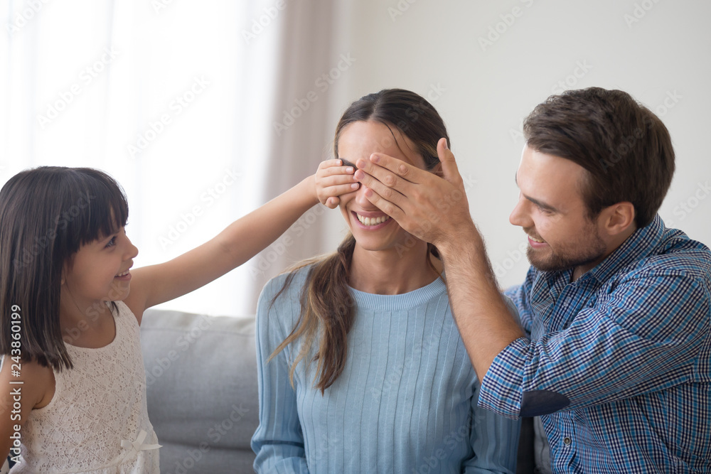Cute kid daughter and loving husband closing eyes of happy mom making unexpected pleasant surprise on mothers day, caring family child and dad congratulating mommy with birthday or holiday at home Cute kid daughter and loving husband closing eyes of happy mom making unexpected pleasant surprise on mothers day, caring family child and dad congratulating mommy with birthday or holiday at home