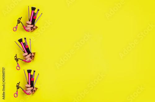 Pattern of woman hands with professional cosmetic tools for make up: brushes, mascara, lipstick, eyelash curler on yellow background. Beauty concept. Banner for cosmetics sale. Copy space