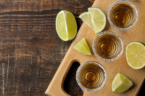 gold tequila in a glass shot glass with salt and lime on a brown wooden background. top view with space for text