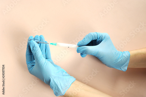 A set of drugs from the ampoule in the syringe. Ampoule in one hand. Syringe for injection in the other hand. Hands of a medical worker in latex gloves. Close-up. Light background.