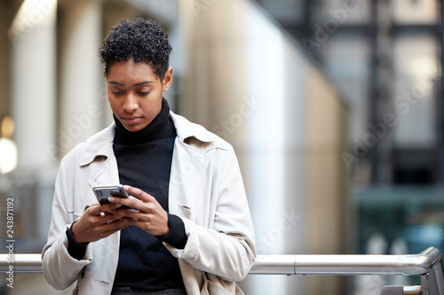Young adult woman standing in a business area of the city using her smartphone, focus on foreground