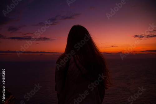 Silhouette of a young woman enjoying beautiful colorful sunset standing above the sea 