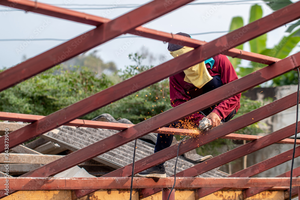 The man wearing brown shirt is cutting or sawing the metal on the roof construction by the metal saw on the top of the house in the sunny day. 