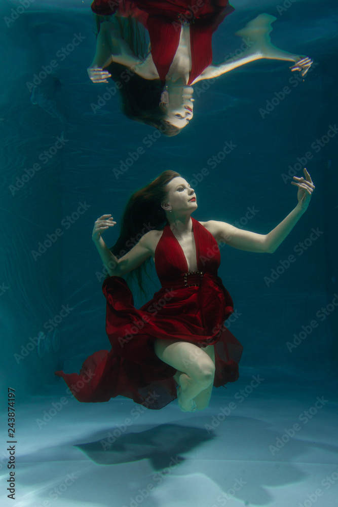 beautiful free diver woman swimming in long red evening dress under water alone in the deep