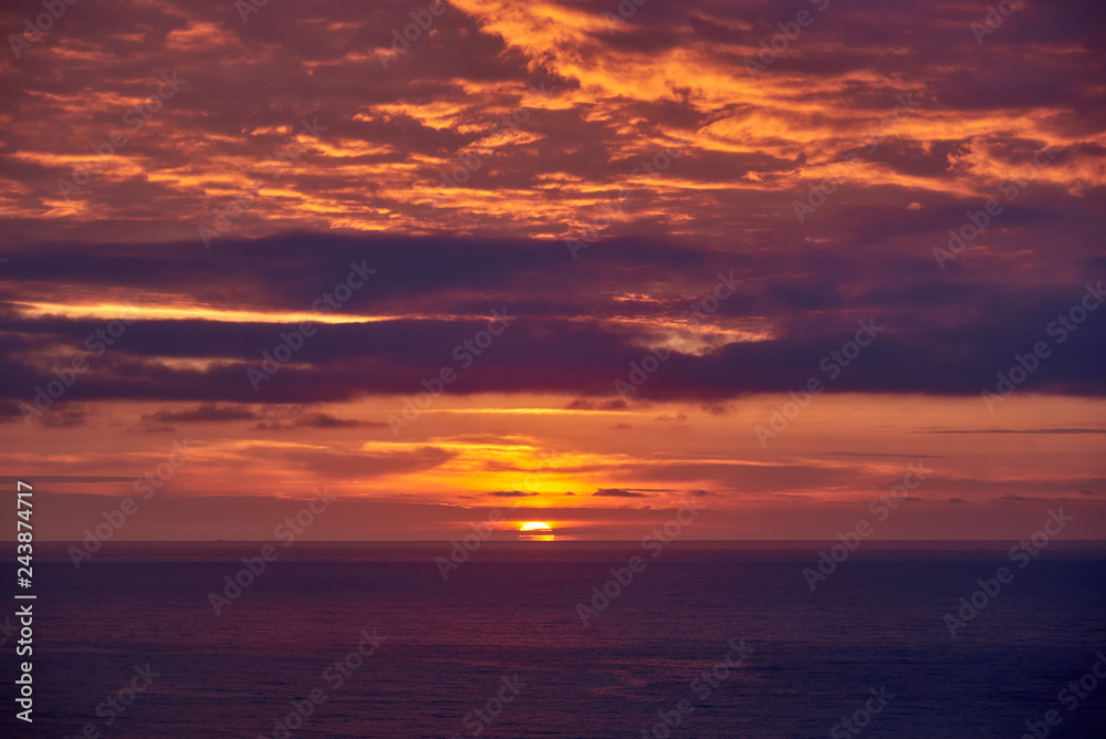 Seashore with violet water and orange purple sky.