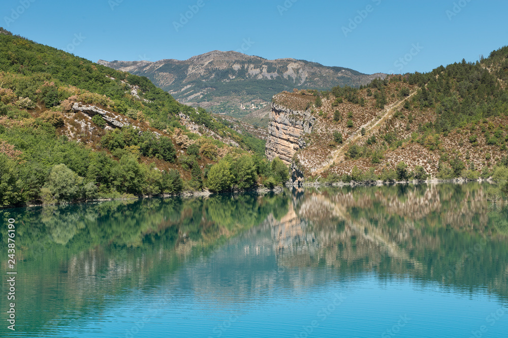 Lake of Castillon, a lake with mountains and green hills with a blue sky