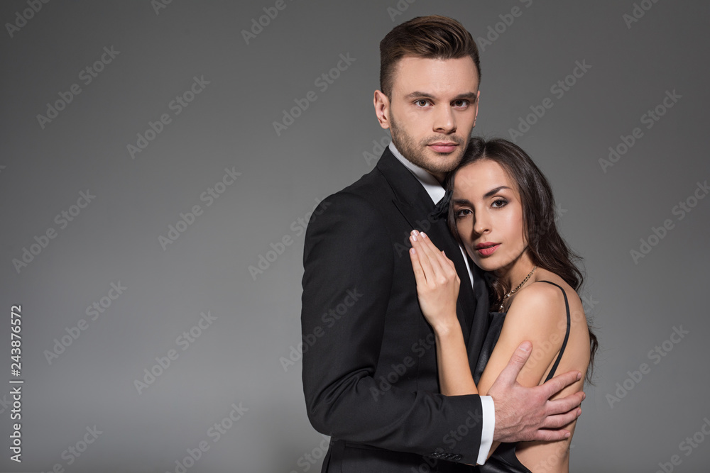elegant couple in black clothes embracing together isolated on grey