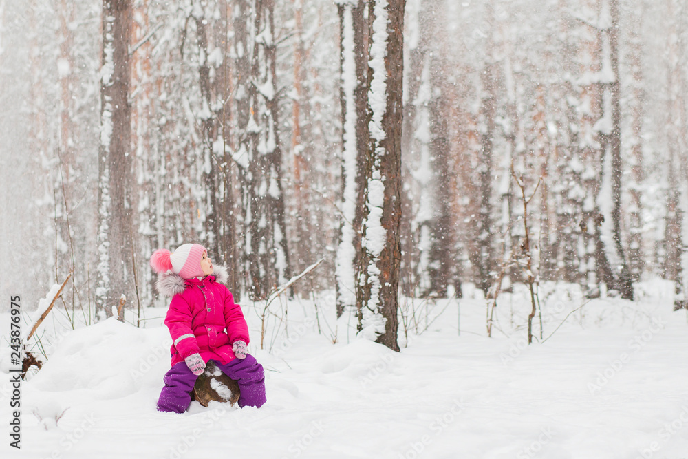 Little girl sitting in the winter pine forest