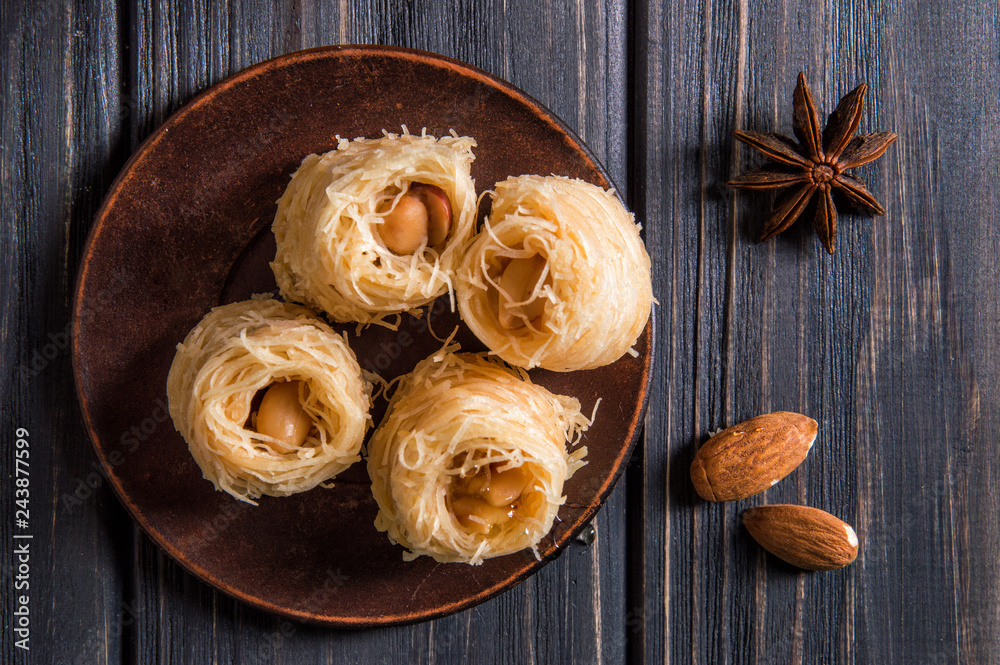 Top view, flat lay. Close up. Turkish traditional sweets on an old clay saucer. Baklava bird's nest. Dark wooden background. Top view, flat lay. Close up. Turkish traditional sweets on an old clay saucer. Baklava bird's nest. Dark wooden background.