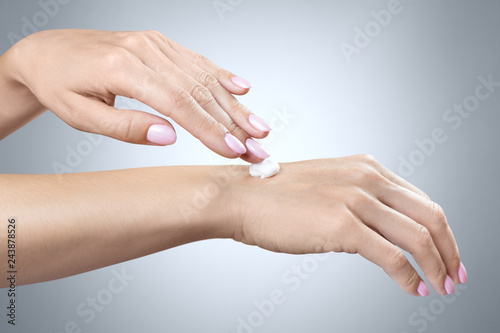 Closeup of beautiful woman hands applying moisturizing hand cream on grey background