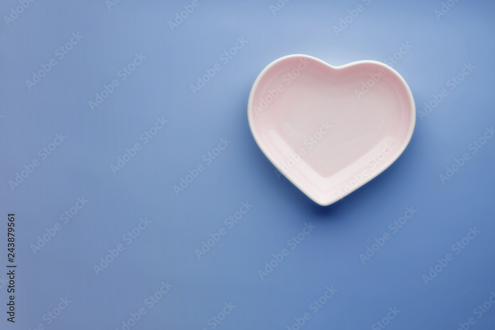 Ceramic glossy heart-shaped plate on a blue background. Stylish tableware. Saucer for Valentine's Day or wedding romantic menu design. Copy space. Close-up. Minimalism. Ceramic glossy heart-shaped plate on a blue background. Stylish tableware. Saucer for Valentine's Day or wedding romantic menu design. Copy space. Close-up. Minimalism.