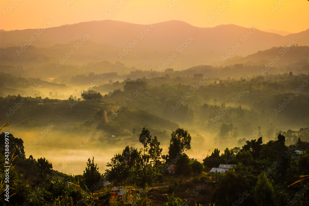 Gentle yellow light and light mist over the hills in country side with traditional houses and the tropical nature of Uganda on the border with the Congo at dawn