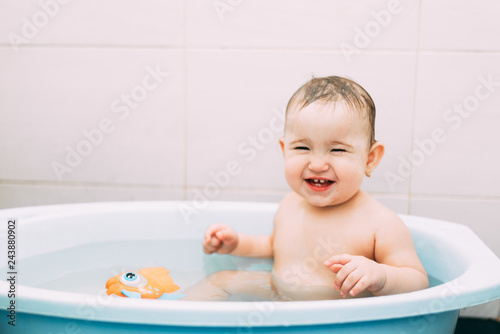 Fotografia little girl baby is bathed in the blue basin in the bathroom is very fun