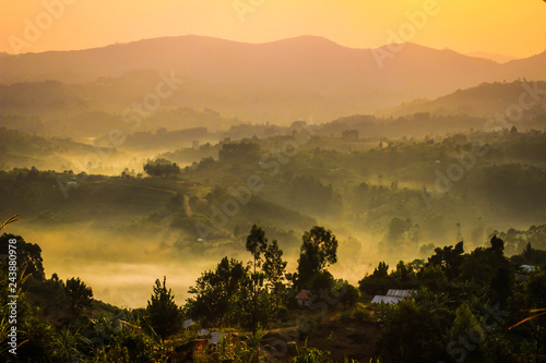 Gentle yellow light and light mist over the hills in country side with traditional houses and the tropical nature of Uganda on the border with the Congo at dawn photo