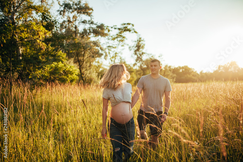 A pregnant woman walks at the forest with her husband.