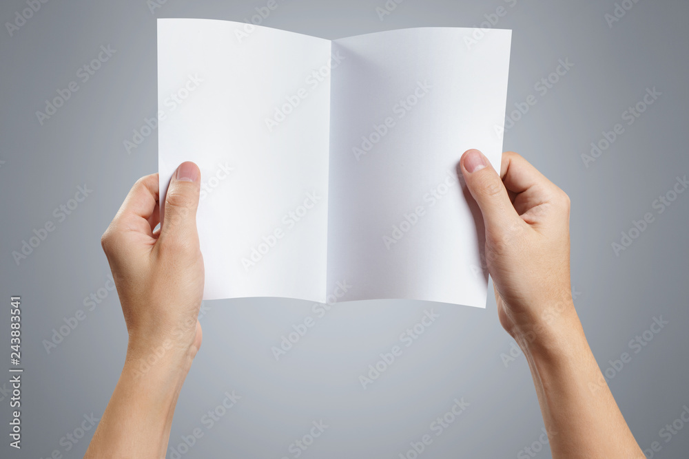 Hands holding a sheet of white paper with fold line in the middle on gray background Hands holding a sheet of white paper with fold line in the middle on gray background