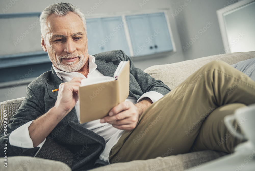 Stylish man in beige trousers and grey suit sitting on sofa