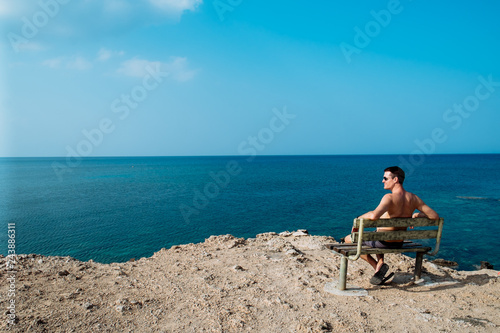 Rear view portrait of white man sitting relaxed on a bench and looking at the sea, man on a holiday. Cyprus © matilda553