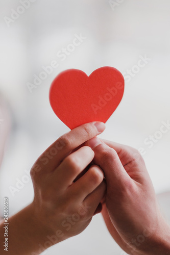 Male and female hands hold a valentine in the form of a paper heart.