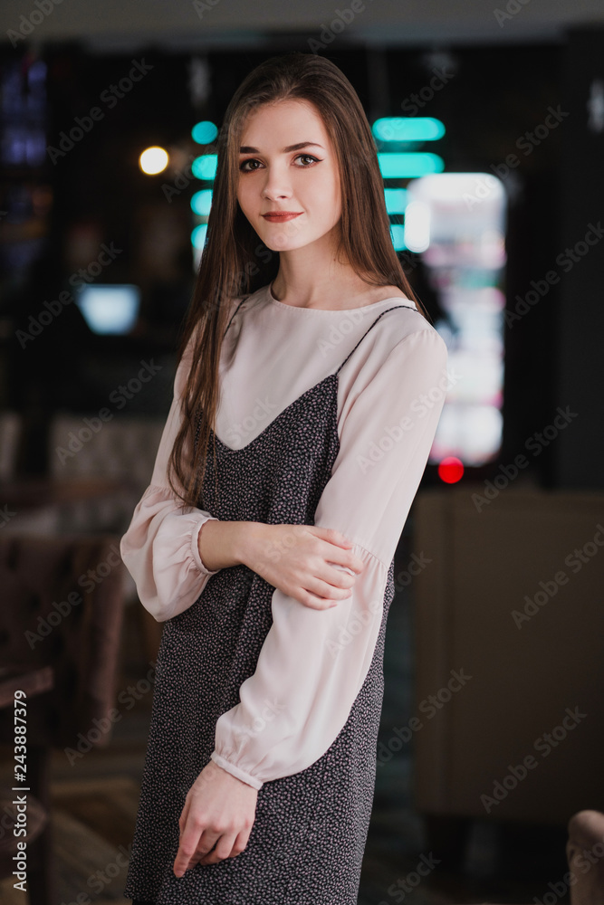 Portrait of a young girl with long hair on the background of luminous signs in the interior of a cafe or restaurant. Black dress and blouse, elegant and attractive.