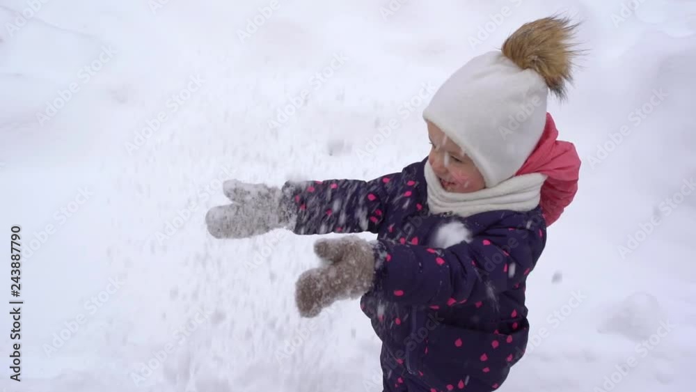 Cute little girl throwing fresh fluffy snow up in air while playing with mother outdoors on cold frosty winter day. Slow motion full hd video footage.