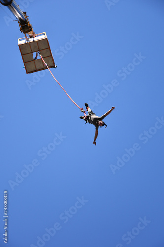 Bungee jumping from a 50-metre-high crane during Sofia Extreme Sports Festival. Seen from the ground man falling down from a platform high in the blue sky