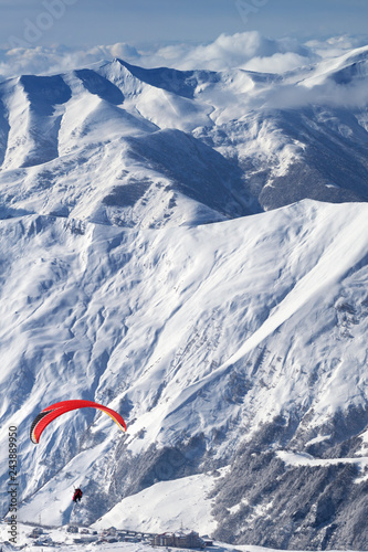 Paragliding at snowy mountains over ski resort at sunny day