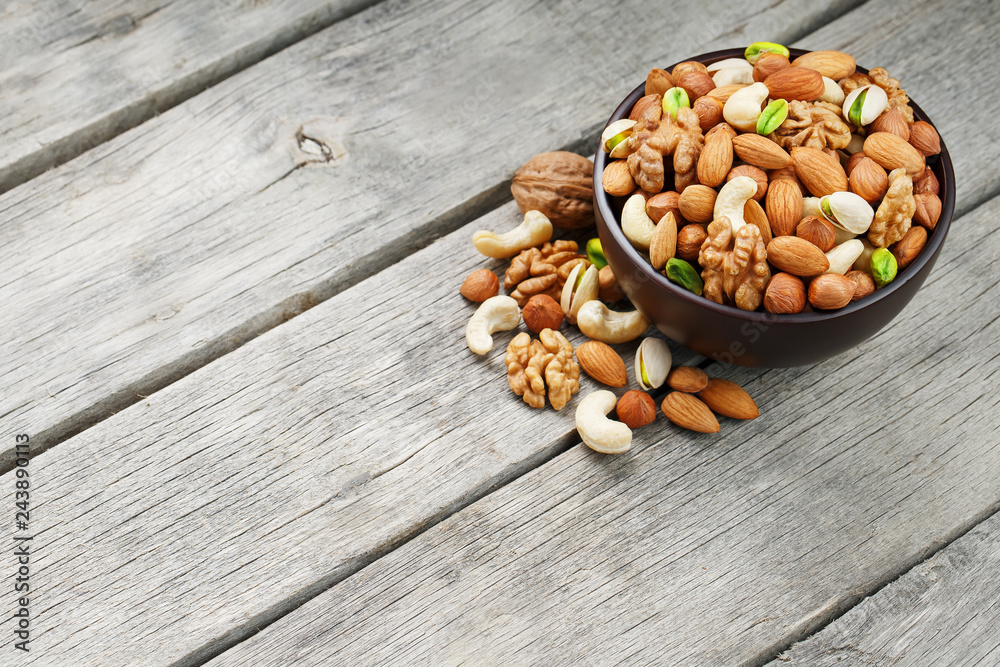 Wooden bowl with mixed nuts on a wooden gray background. Walnut, pistachios, almonds, hazelnuts and cashews, walnut.