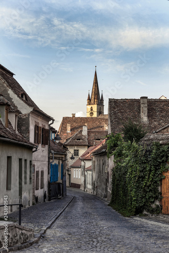 sibiu old city street with cobblestone pavement and church tower on background