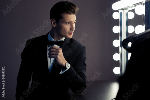 Young gentleman in black suit looking at mirror, preparing to wedding