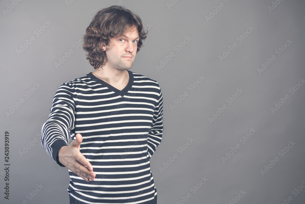 Welcome, nice to see you. Man in black and white striped sweater looking at camera with reaching out his hand offering handshake. Indoor studio shot. Hello, greeting gesture. Human emotions and signs. Welcome, nice to see you. Man in black and white striped sweater looking at camera with reaching out his hand offering handshake. Indoor studio shot. Hello, greeting gesture. Human emotions and signs.